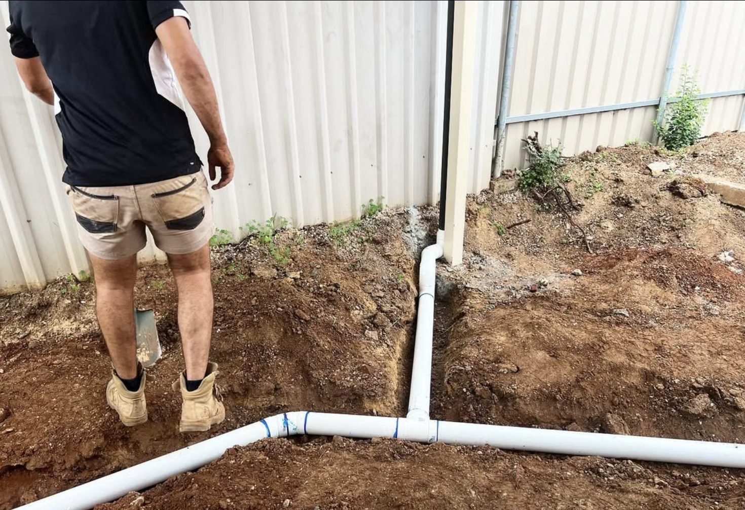 New PVC stormwater drainage pipework laid in a trench beside a colorbond fence
