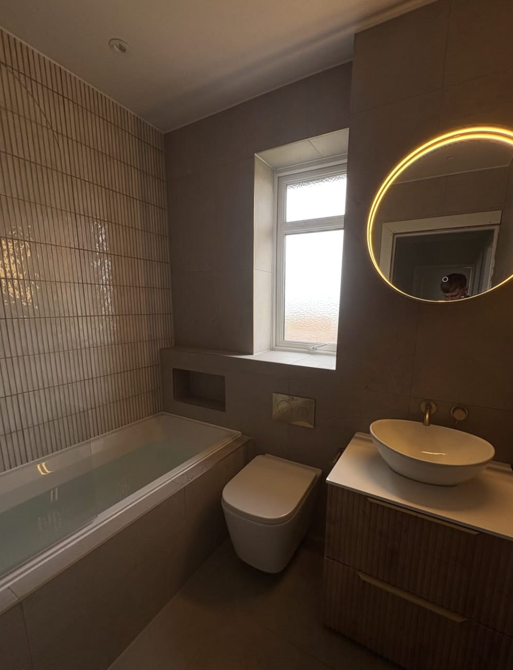 Bathroom with fluted wall tiles, wall hung toilet, vessel basin and round backlit mirror
