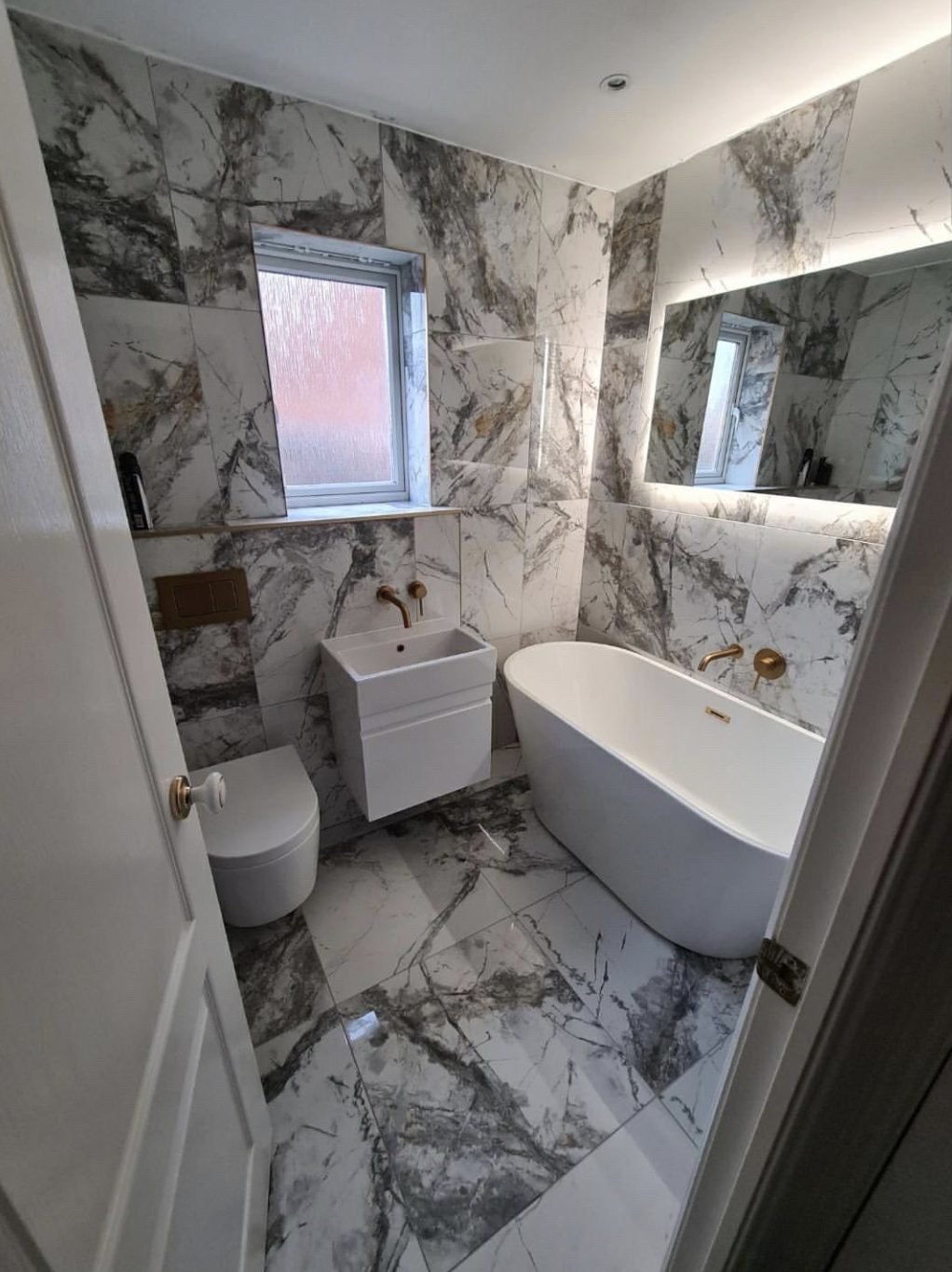 Marble tiled bathroom with freestanding bath, wall hung toilet and brushed gold tapware
