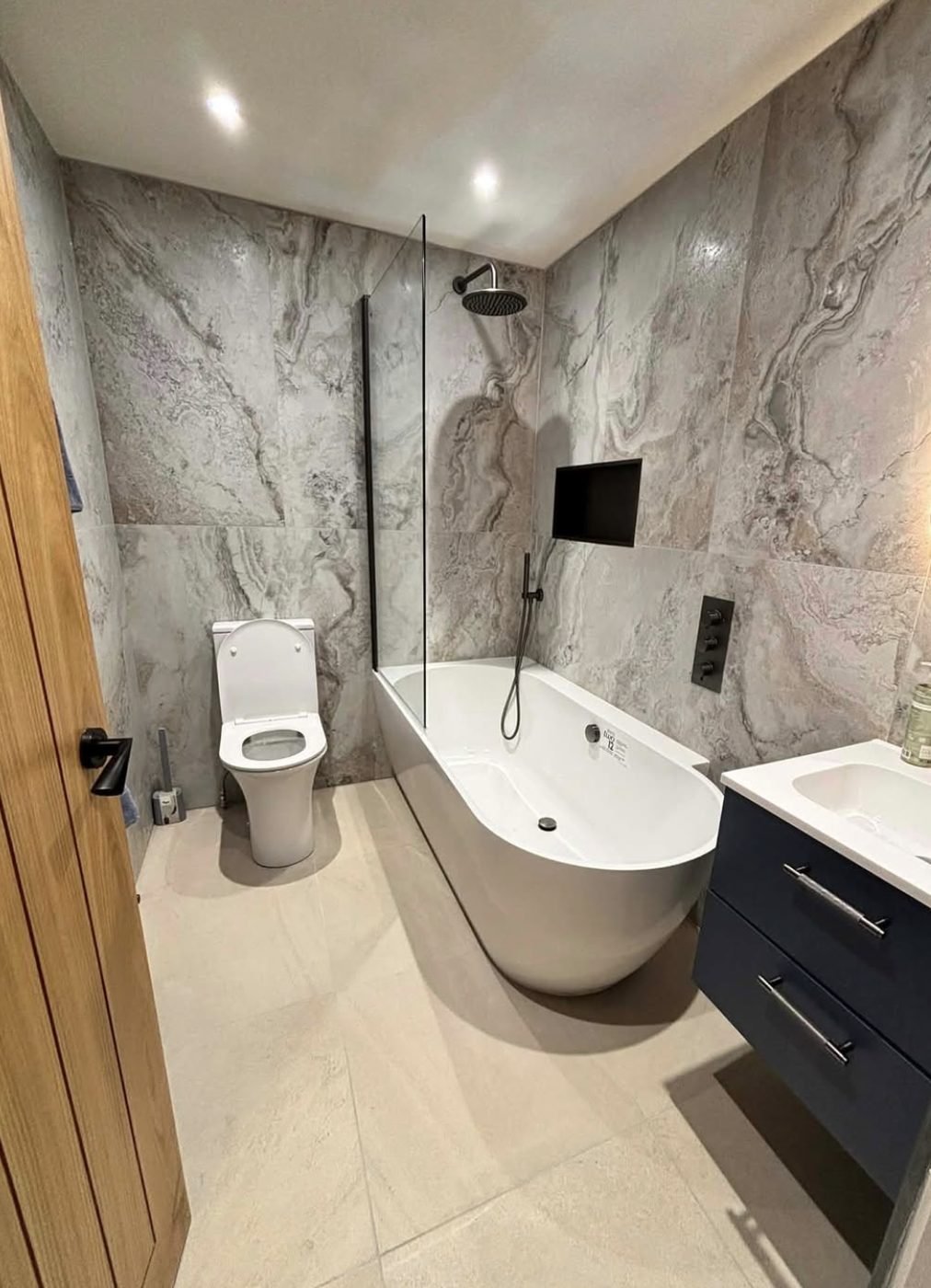 Marble tiled bathroom with a shower over bath, black tapware and navy vanity