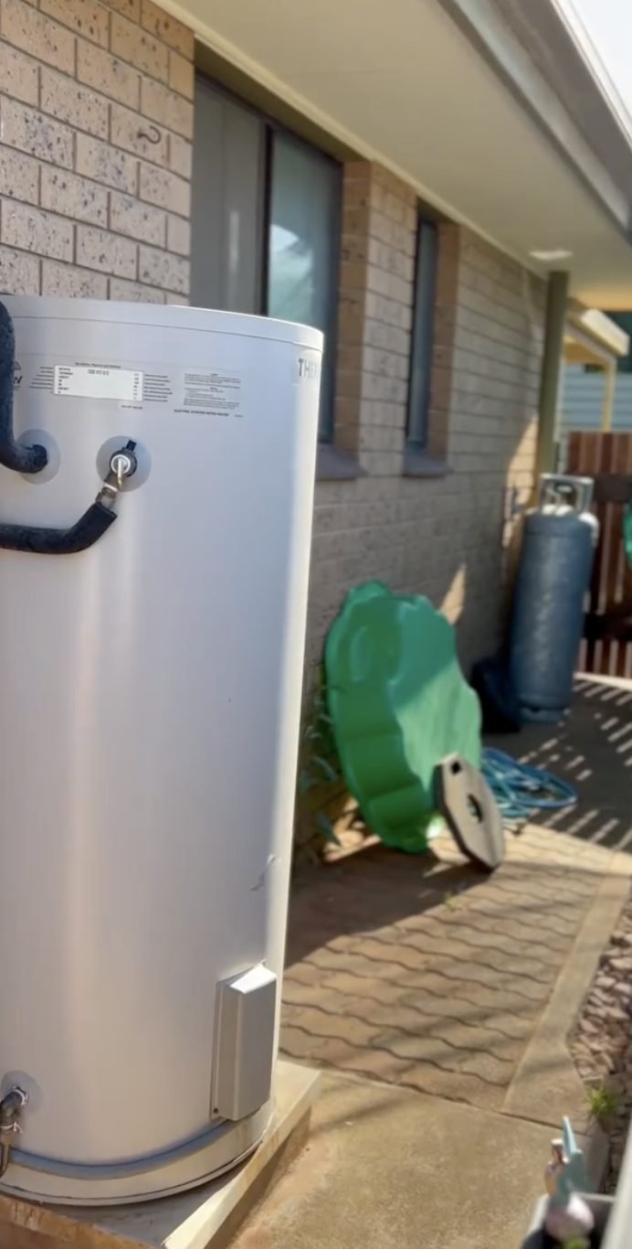 Electric storage hot water system installed outside a brick and tile home