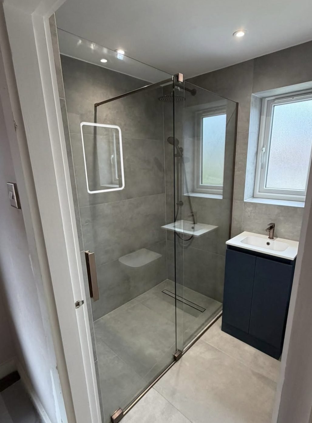 Walk in shower with a linear floor waste, glass screen and navy vanity unit